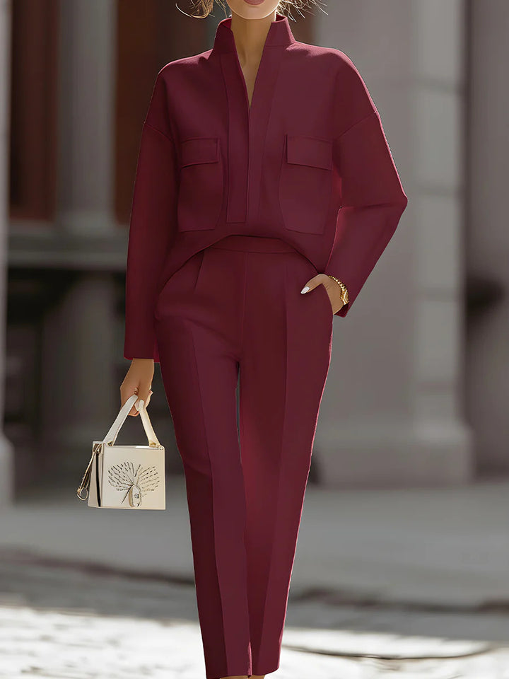 Person wearing a burgundy suit holding a small handbag in an outdoor setting.
