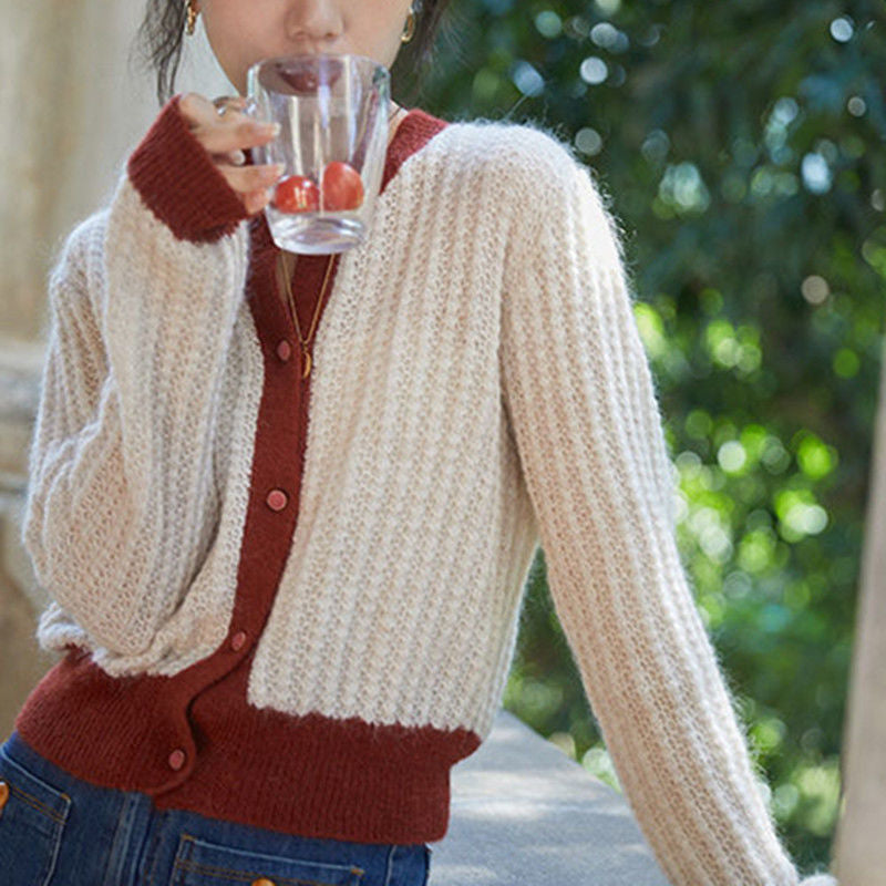 Person wearing a beige and red cardigan holding a glass with cherries outdoors.