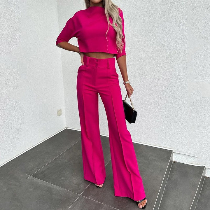 Person wearing a bright pink outfit with wide-leg pants and a matching top, standing in a minimalistic room.