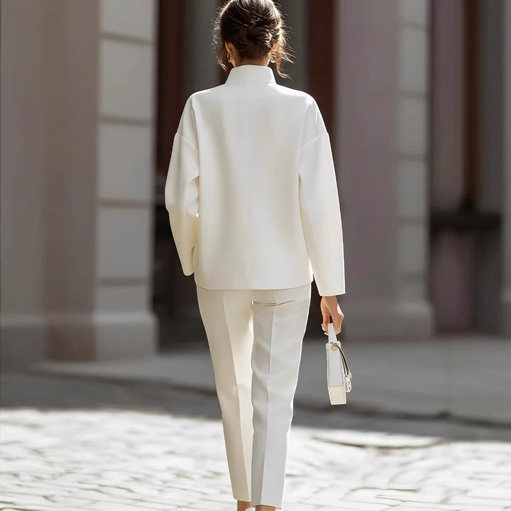 Woman in a white suit walking on a street with classical architecture in the background