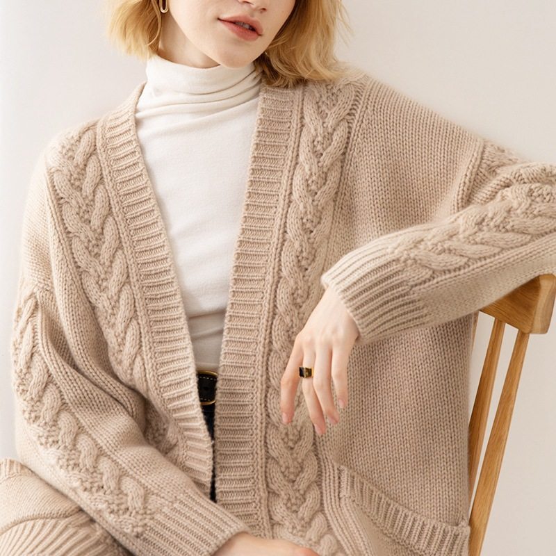 Person wearing a beige cable knit cardigan over a white turtleneck.