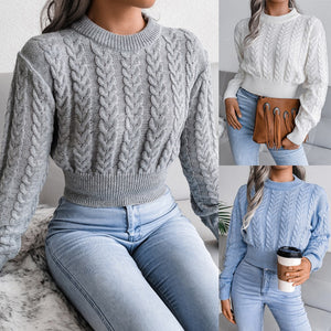 Woman wearing a gray cable knit sweater and light blue jeans, holding a brown bag.