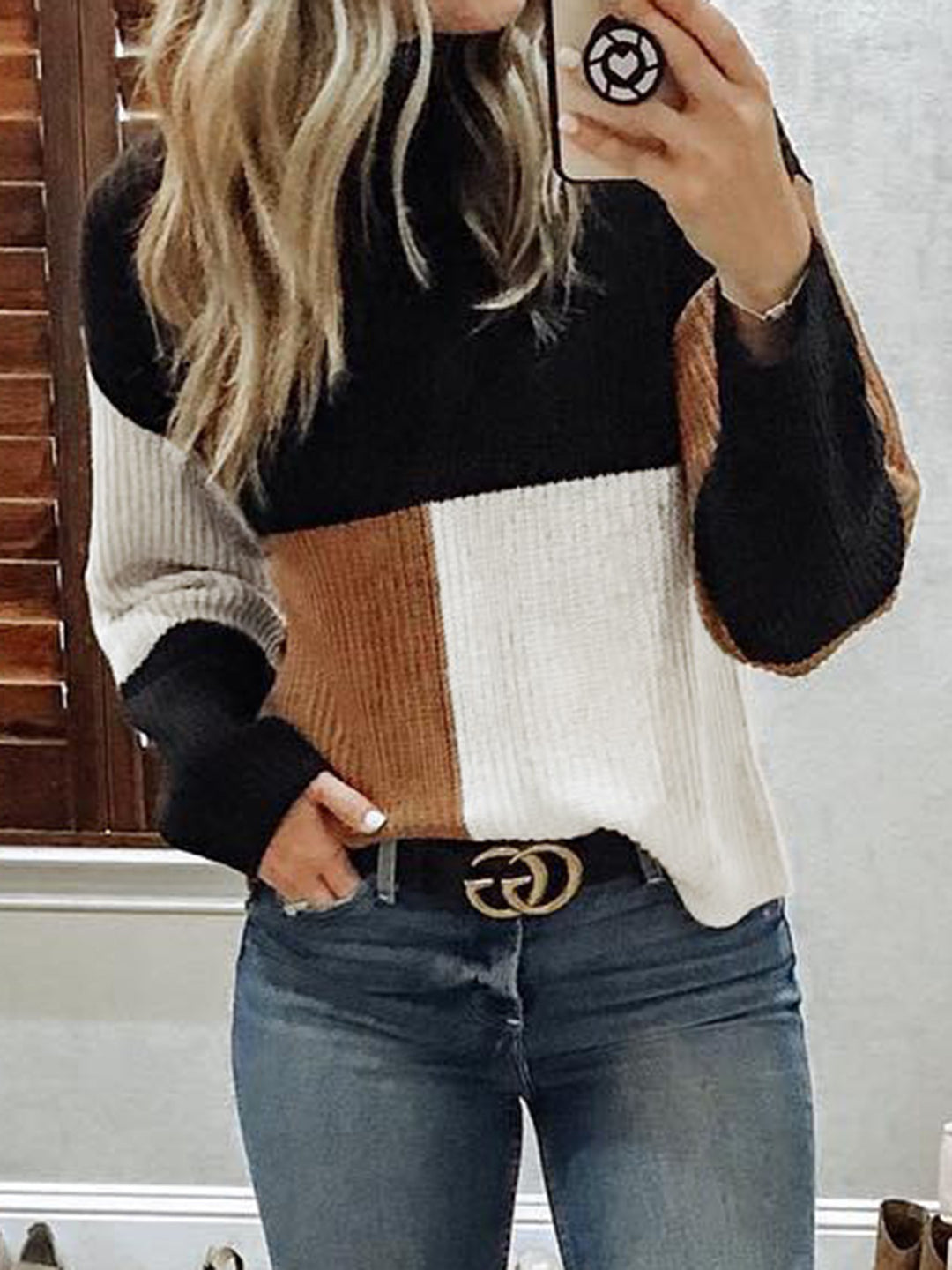 Person wearing a black, brown, and white sweater with blue jeans.