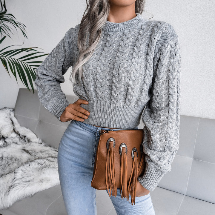 Person wearing a gray cable knit sweater and light blue jeans, holding a brown leather bag with fringes.