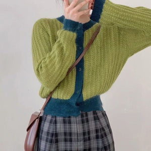 Person wearing a green and blue sweater with plaid skirt against a plain background