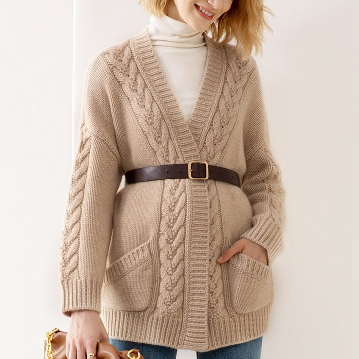 Person wearing a beige cable knit cardigan with a brown belt against a white background