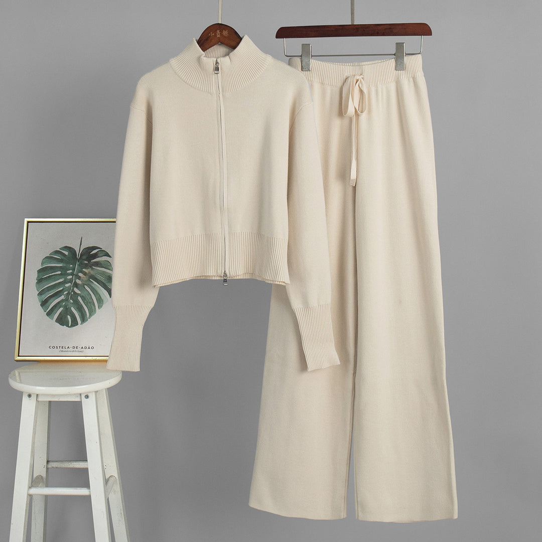 Beige sweater and pants set on hangers against a gray background with a stool and framed picture.