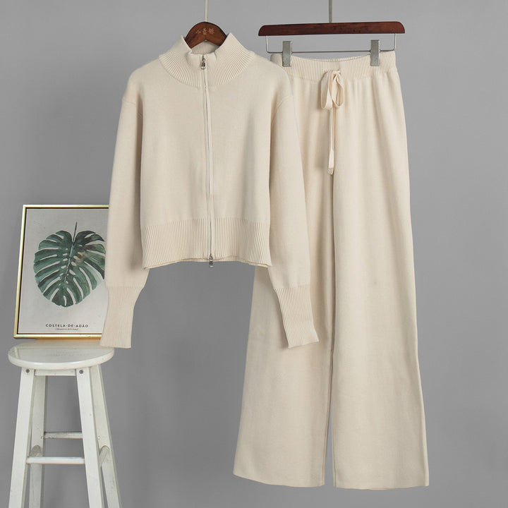 Beige sweater and pants set on hangers against a gray background with a stool and framed picture.