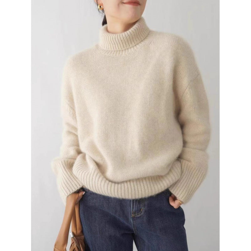 Person wearing a beige sweater and blue jeans against a plain background