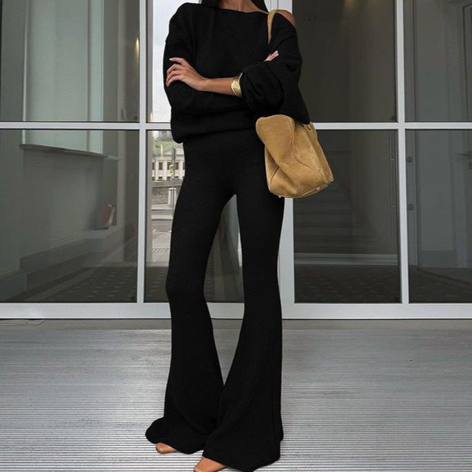 Person wearing a black outfit with a beige handbag standing in front of a glass door.