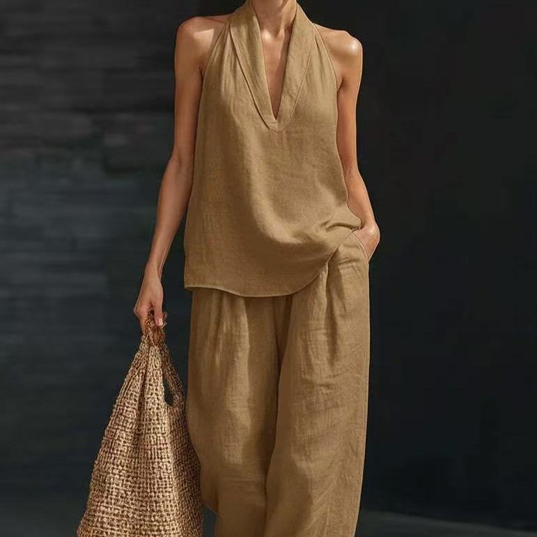 Person wearing a beige sleeveless top and pants holding a woven bag against a dark background