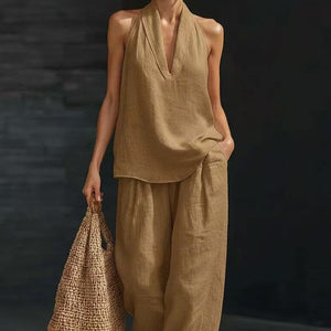 Person wearing a beige sleeveless top and pants holding a woven bag against a dark background