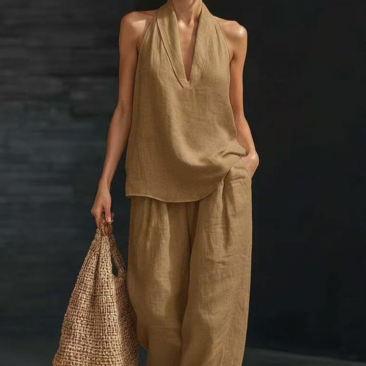 Person wearing a beige sleeveless top and pants holding a woven bag against a dark background