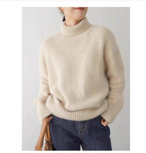 Person wearing a beige turtleneck sweater and blue jeans on a plain background