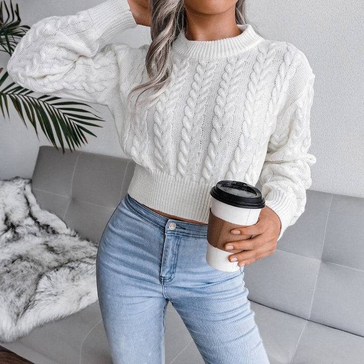 Person wearing a white cable knit sweater and blue jeans, holding a coffee cup.