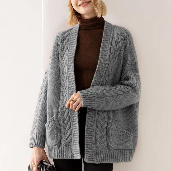 Person wearing a gray cable knit cardigan against a plain background