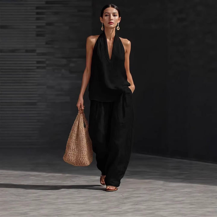 Woman in a black outfit holding a woven bag against a dark background