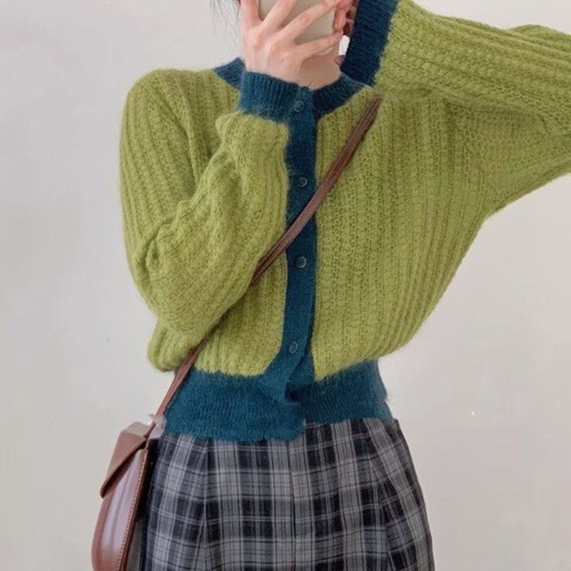 Person wearing a green and blue sweater with plaid skirt against a plain background