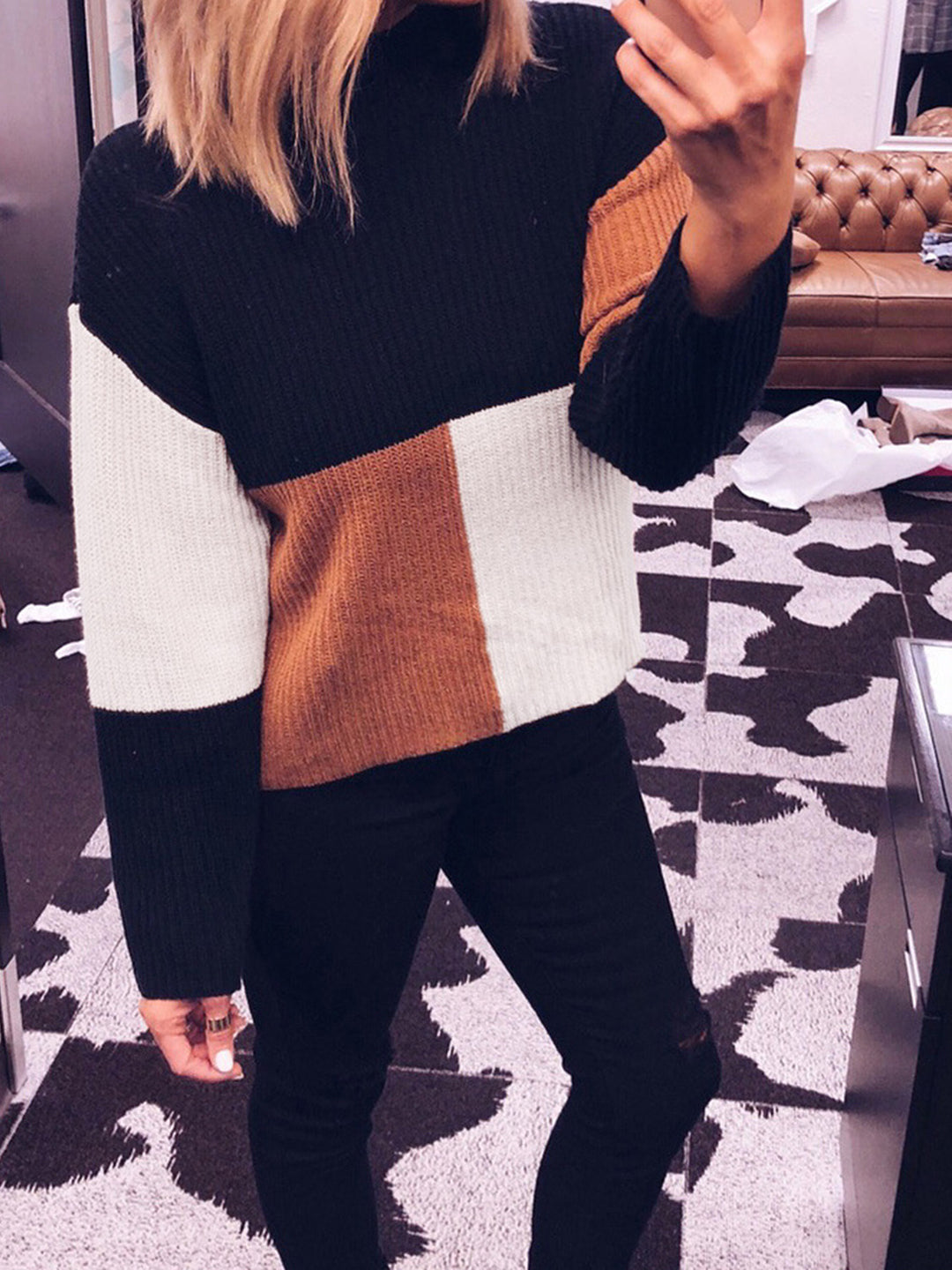 Person wearing a black, white, and brown color-blocked sweater in an indoor setting.