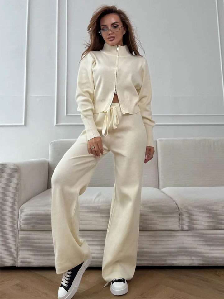 Woman in a cream-colored outfit standing in a modern living room.