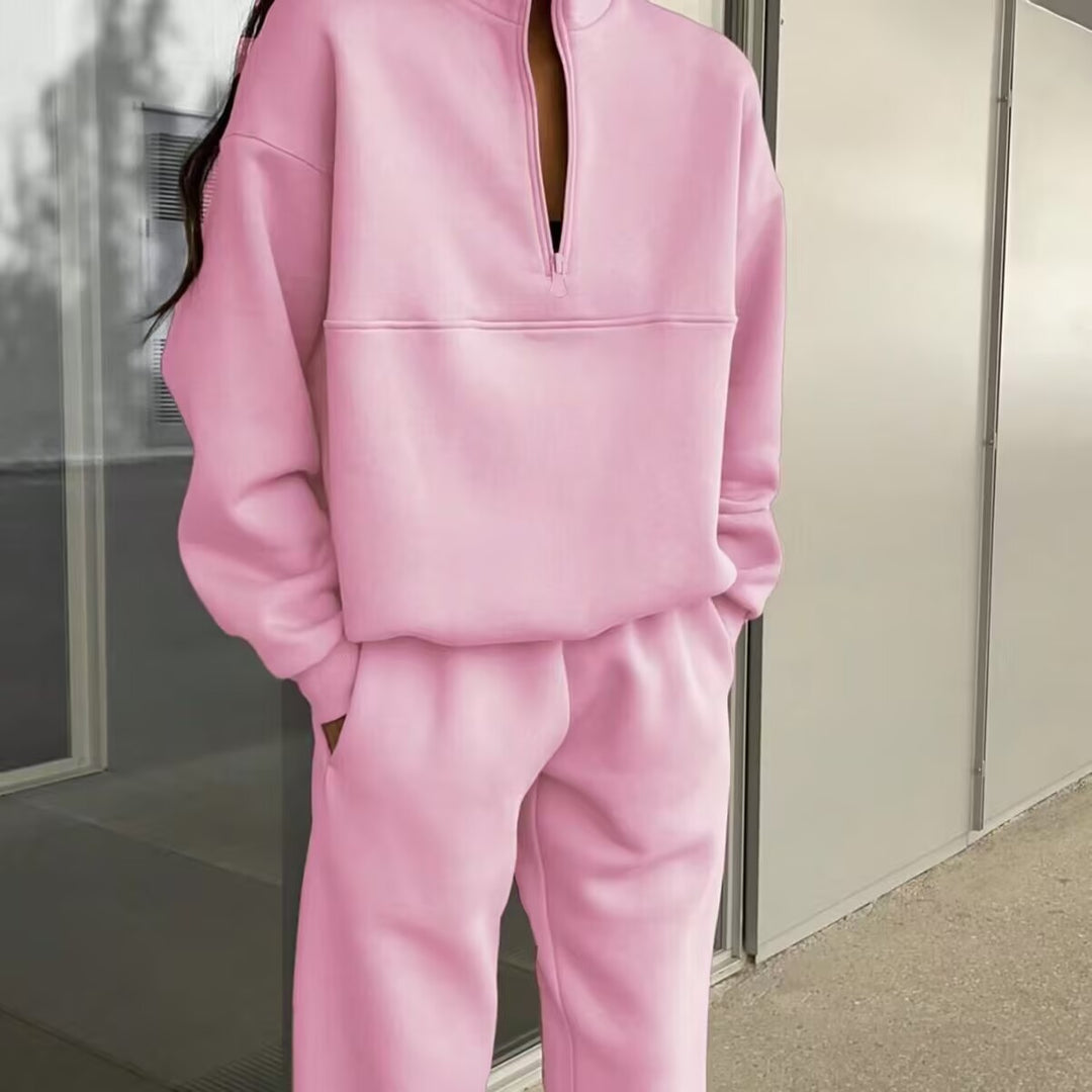 Person wearing a pink tracksuit standing against a neutral wall.
