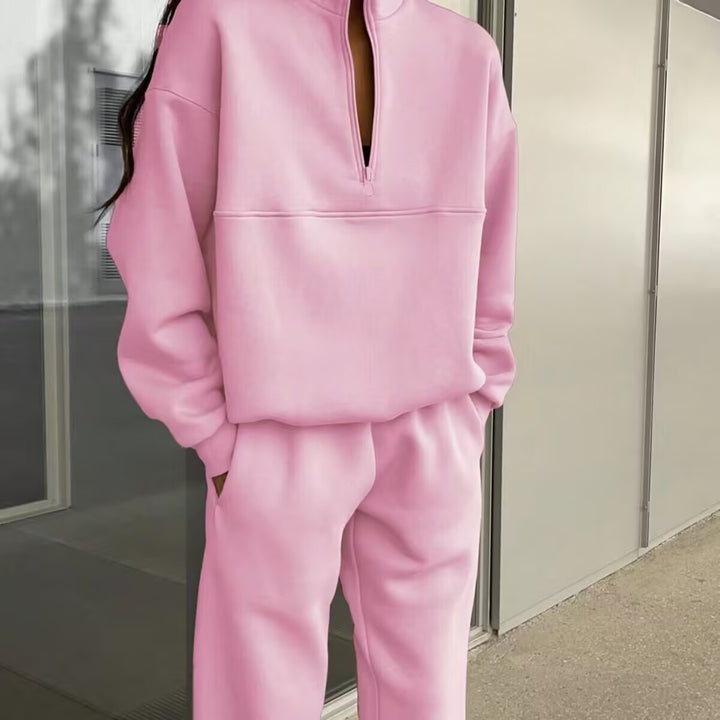 Person wearing a pink tracksuit standing against a neutral wall.