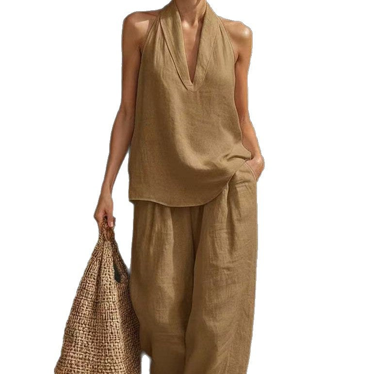 Person wearing a beige sleeveless top and wide-leg pants holding a woven bag on a white background