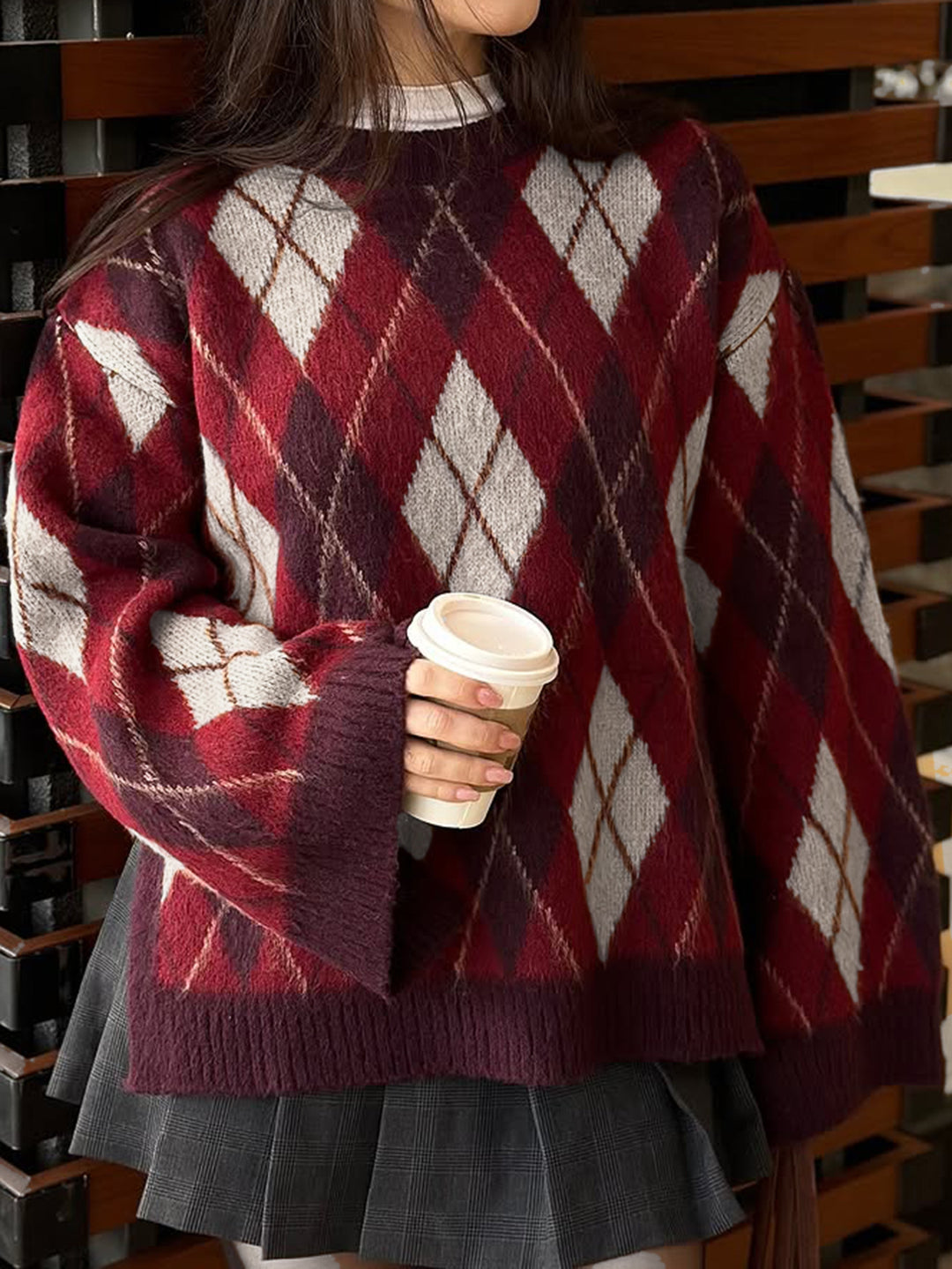 Person wearing a red and white patterned sweater holding a coffee cup.