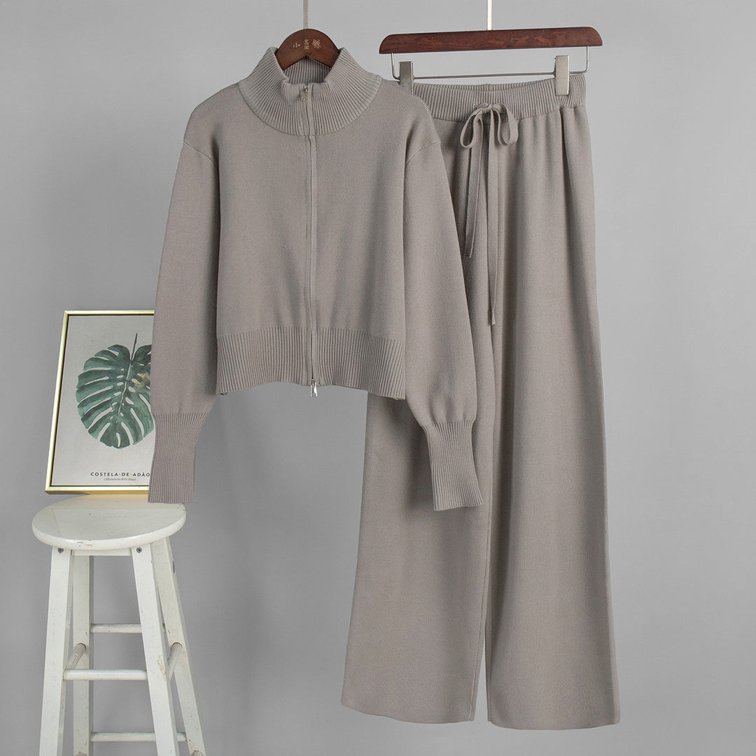 Gray sweater and pants set on hangers with a stool and framed picture in the background.