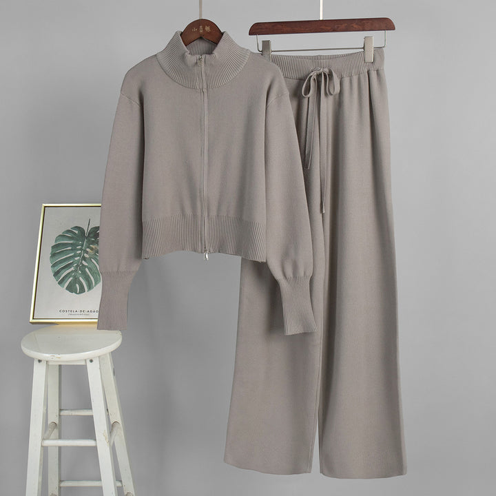 Gray sweater and pants set on hangers with a stool and framed picture in the background.