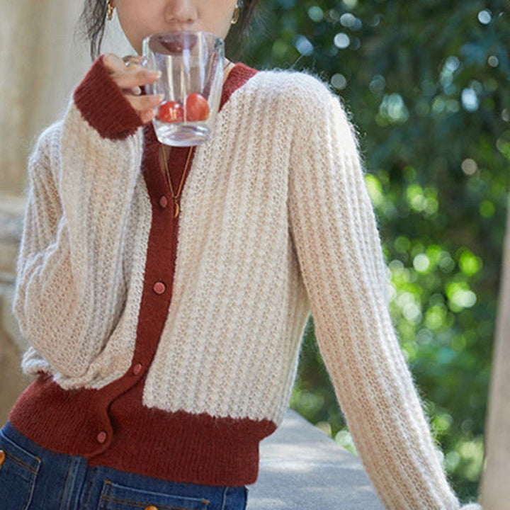 Person wearing a beige and red cardigan holding a glass with cherries outdoors.