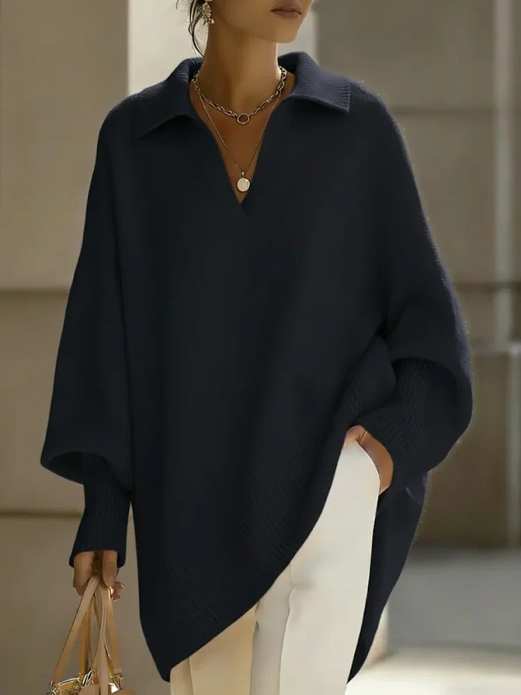 Person wearing a navy blue poncho over a brown top and white pants, holding a beige handbag.