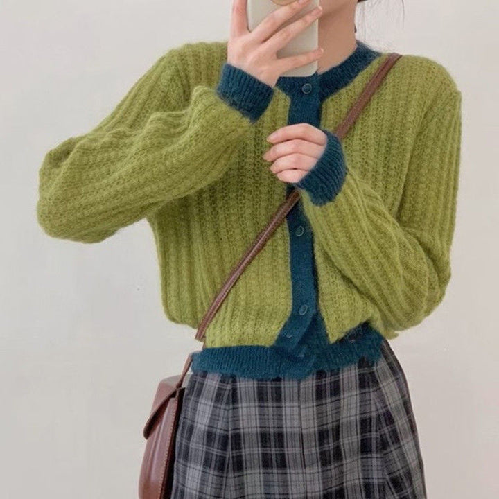 Person wearing a green and blue cardigan with a plaid skirt and carrying a brown bag.